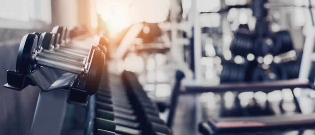 Rangée d'haltères noirs sur un support dans une salle de sport moderne, avec un fond flou lumineux. Équipement de musculation prêt pour l'entraînement.